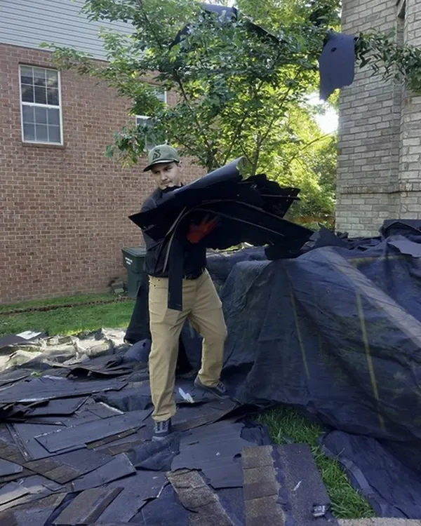 A Hisway team member carrying an armful of old shingles across the tarps