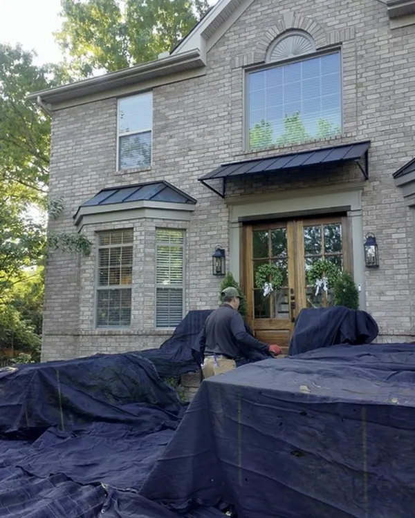 Black protective covers draped over the shrubs and beds in front of a brick home