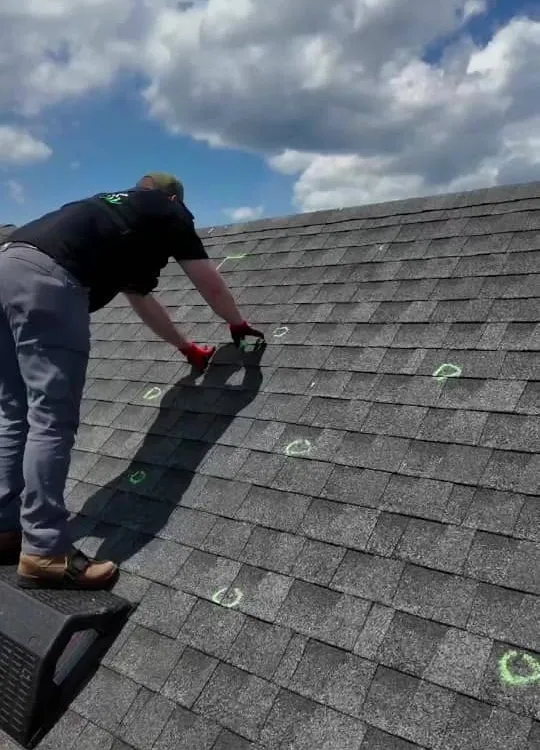 A Hisway inspector on a roof circling hail hits in green chalk