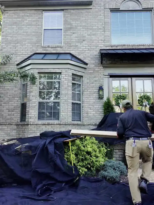 The Hisway crew laying tarps and boards over the beds and shrubs in front of a brick home
